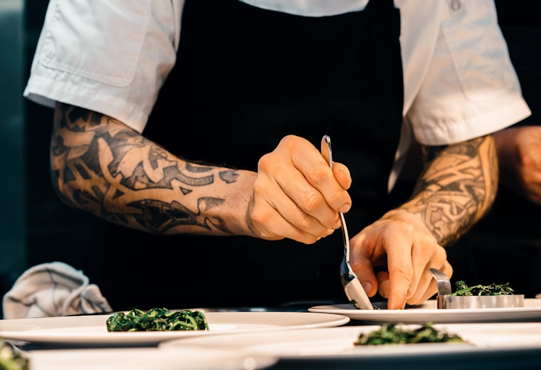 A cook plating greens by hand with tweezers