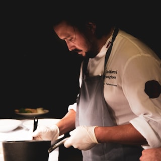 A chef working over a pan in a dark kitchen